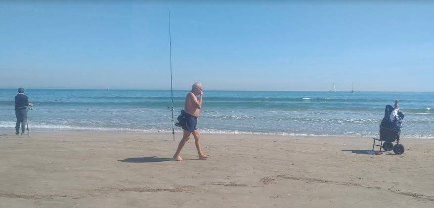 Pie de foto 2: Un hombre pasea tranquilo por la playa mientras otro pesca, indiferentes al clima de histeria general.